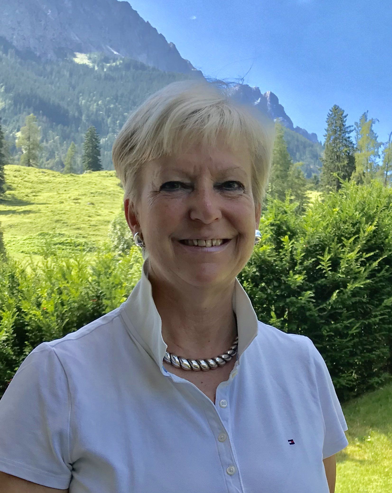Eine Frau in einem weißen Hemd und einer Halskette lächelt vor einem Berg.