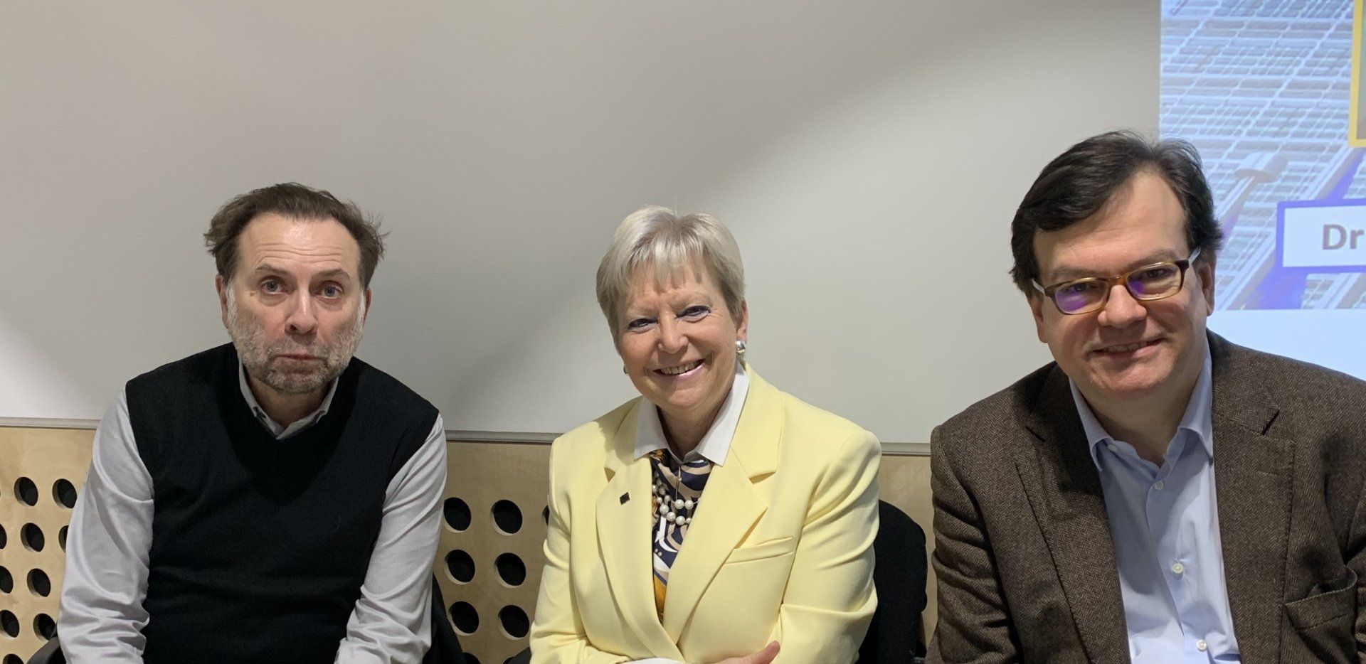 Drei Personen sitzen nebeneinander auf einem Sofa.