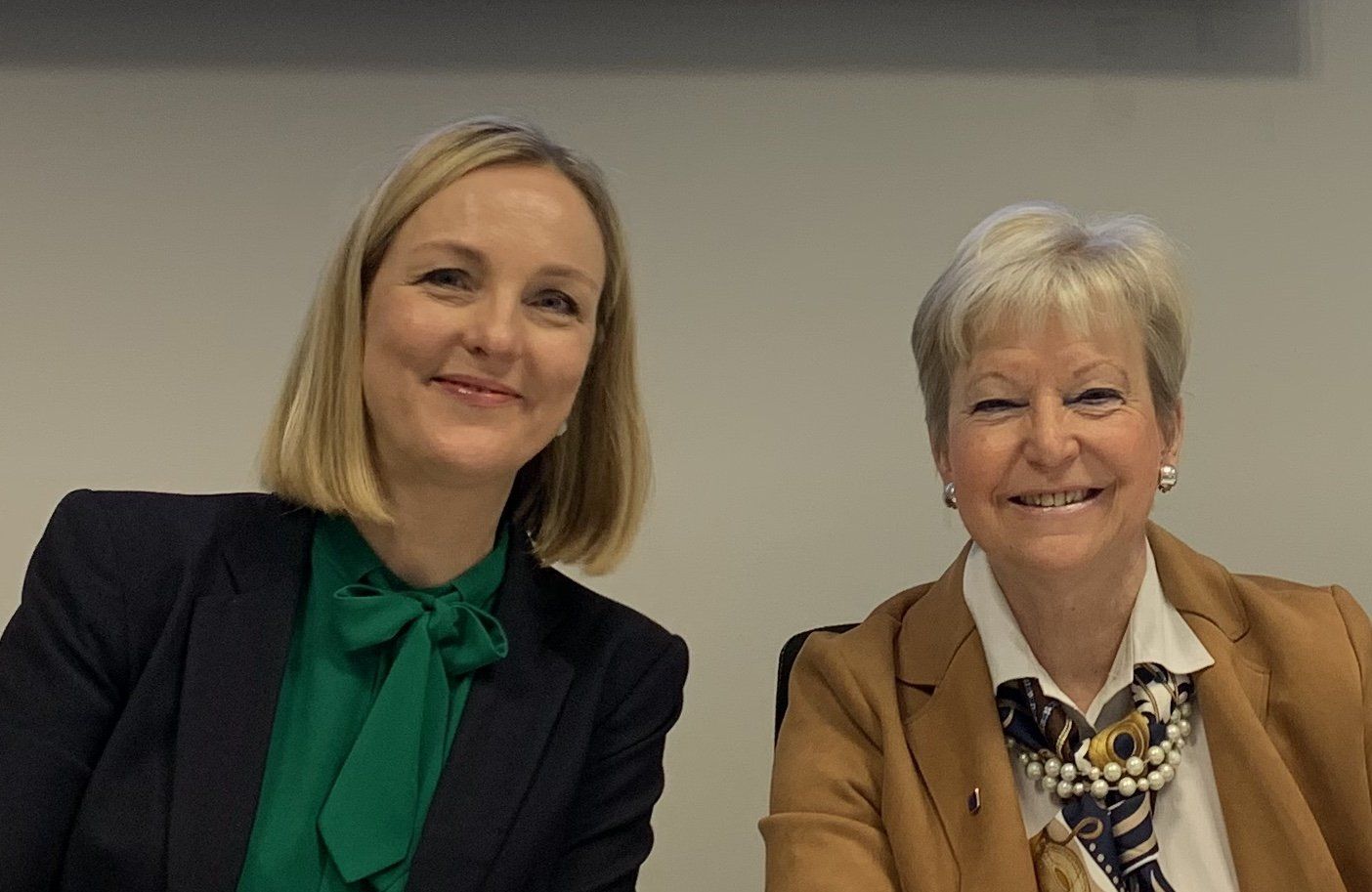 Zwei Frauen sitzen nebeneinander und lächeln in die Kamera.