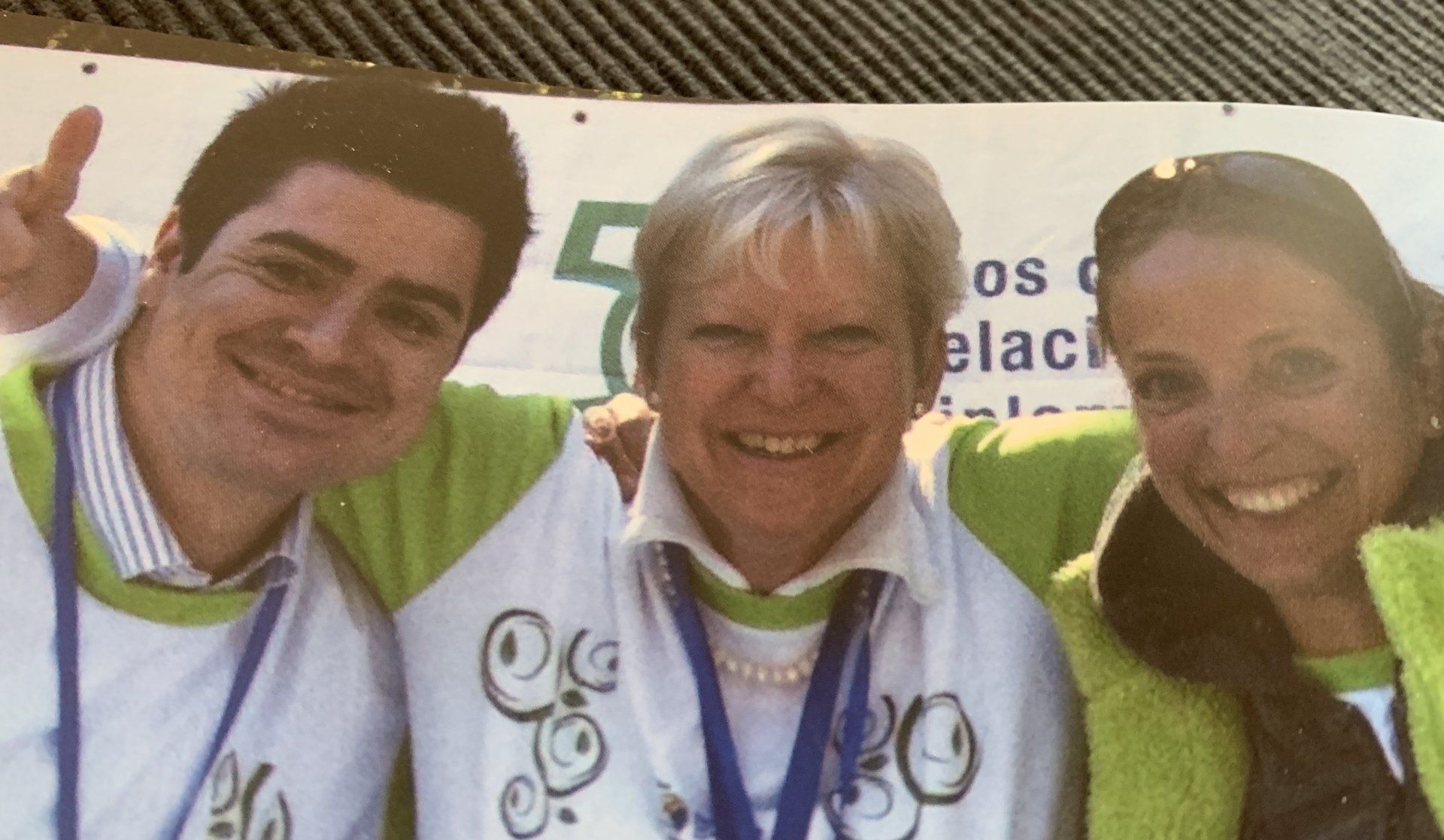 Ein Mann und zwei Frauen posieren für ein Foto vor einem Schild mit der Aufschrift „OS“