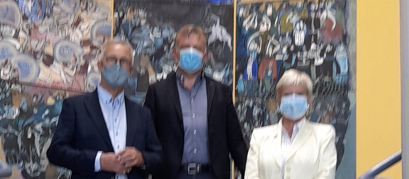 Drei Menschen mit Gesichtsmasken stehen vor einem Gemälde.