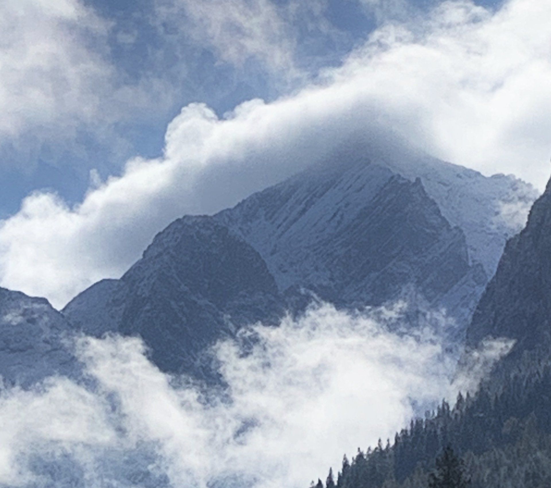 Ein schneebedeckter Berg mit Wolken und Bäumen im Vordergrund