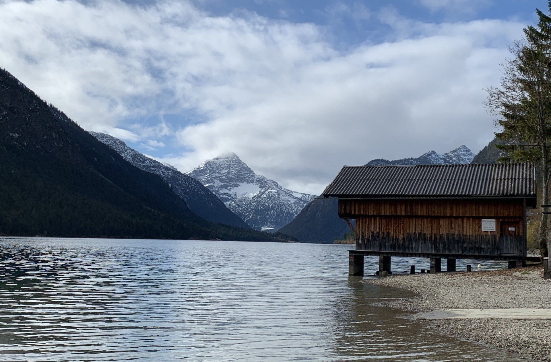 Ein kleines Haus liegt am Ufer eines Sees mit Bergen im Hintergrund