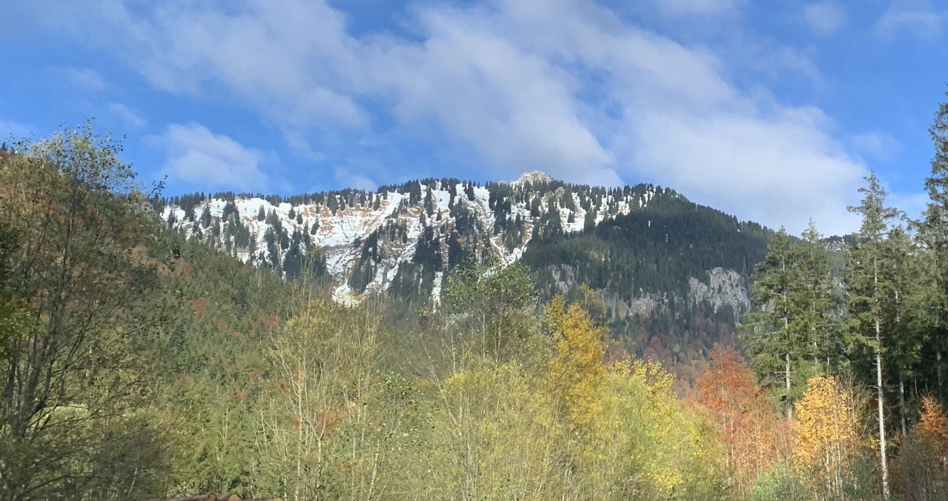 An einem sonnigen Tag ist ein schneebedeckter Berg von Bäumen umgeben.