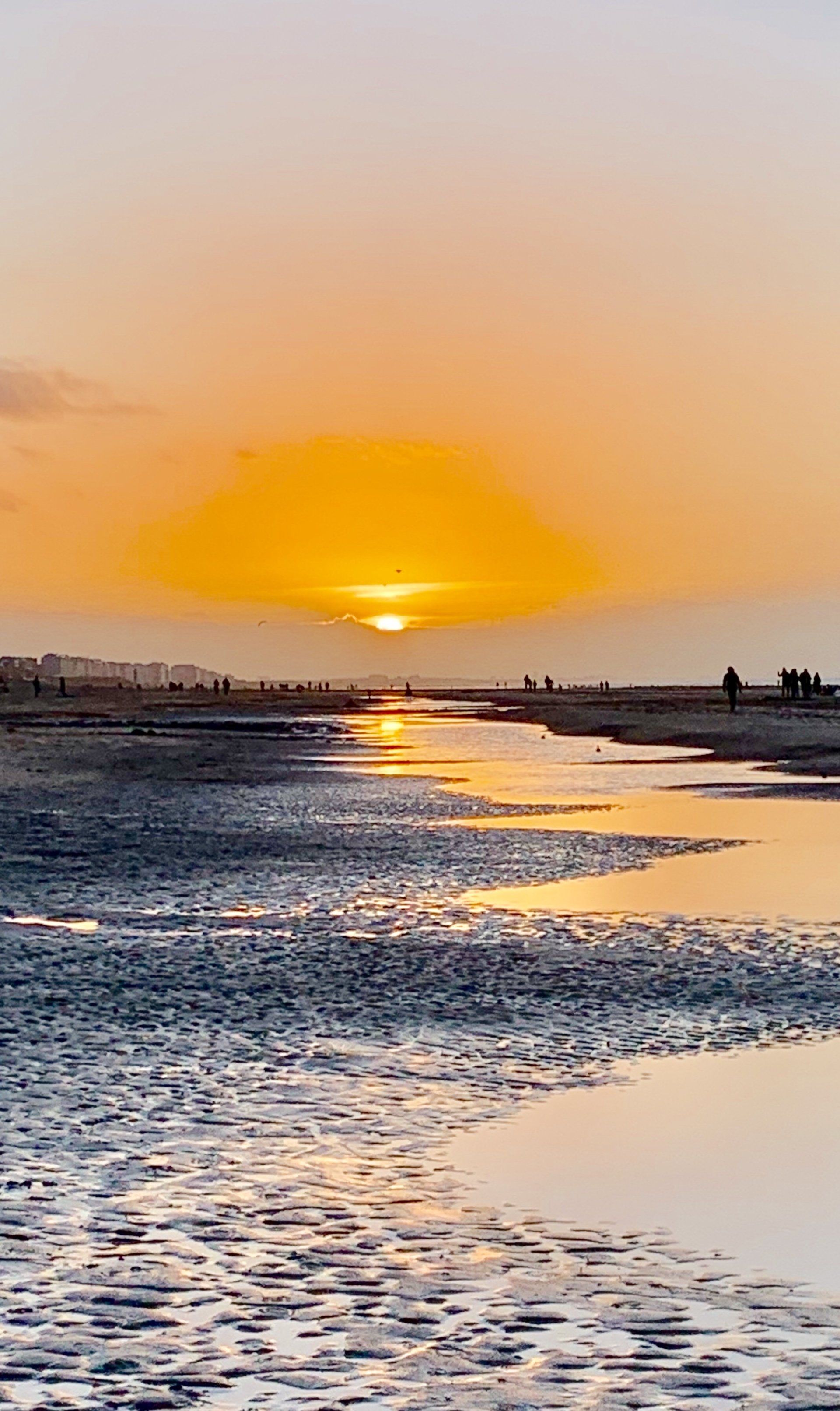 Ein Sonnenuntergang über einem Gewässer mit Menschen, die am Strand spazieren gehen.