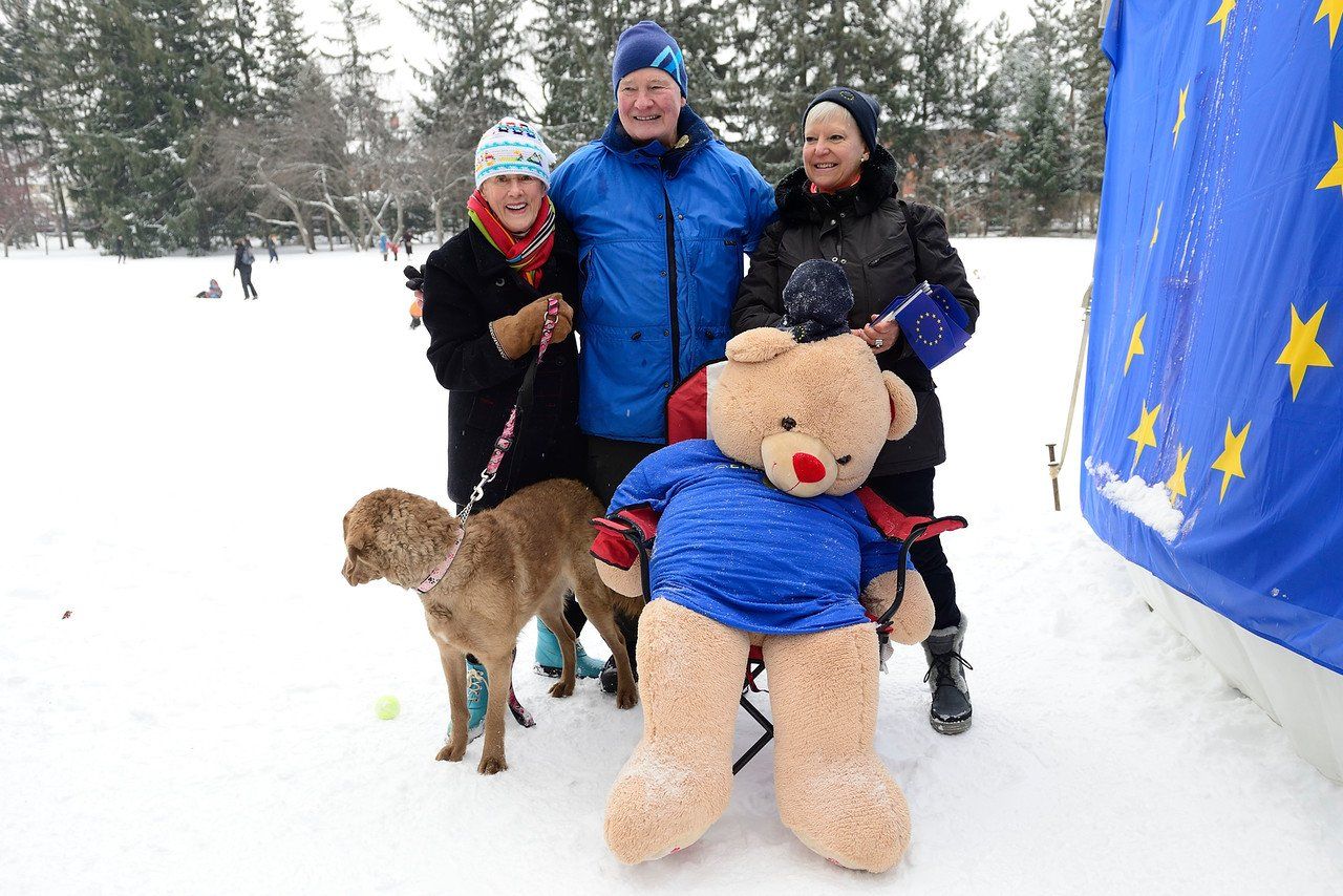 Eine Gruppe von Menschen steht mit einem Teddybären und einem Hund im Schnee.