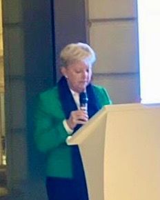 Eine Frau in einer grünen Jacke steht an einem Podium und hält ein Mikrofon.