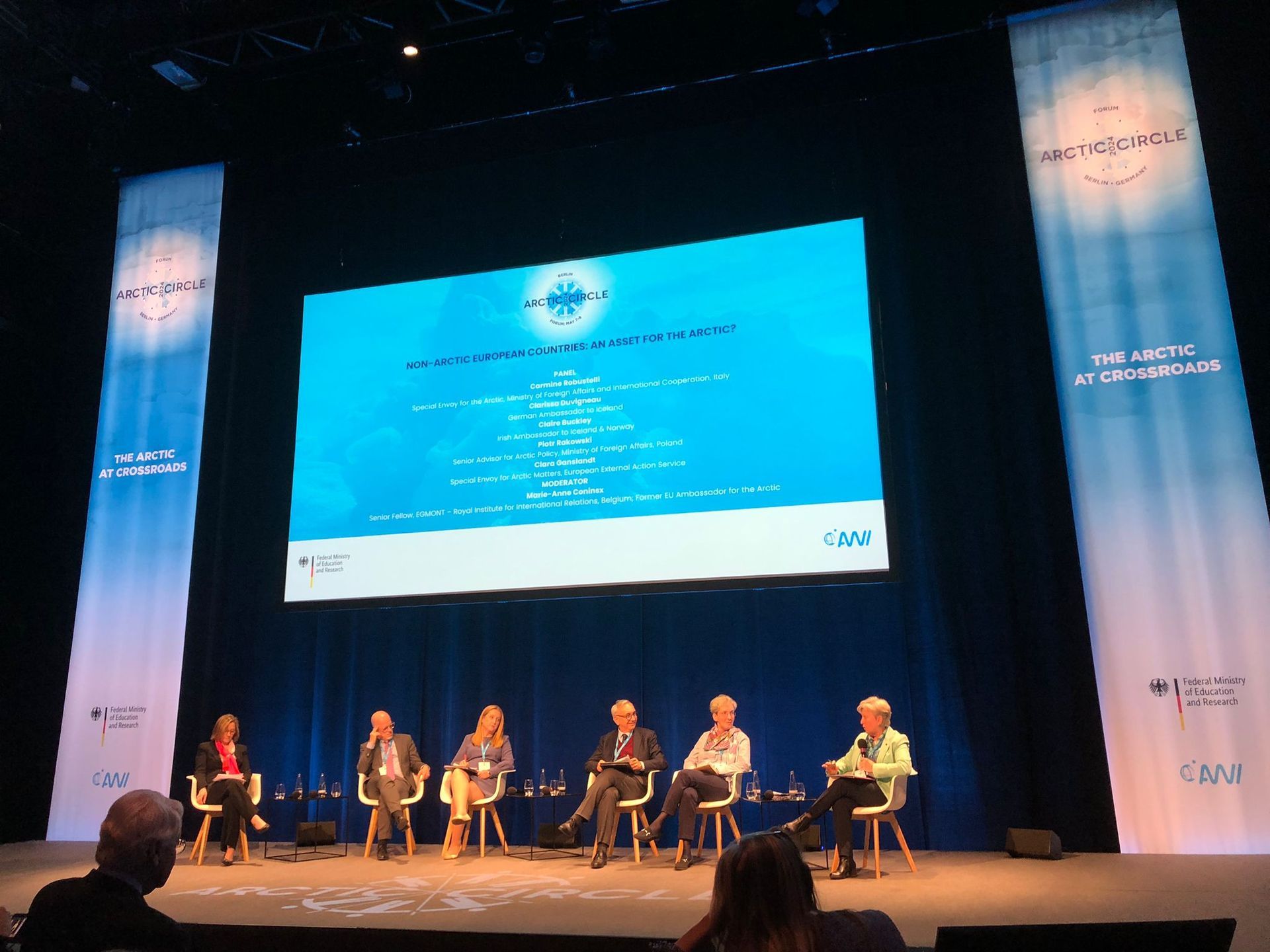 Eine Gruppe von Menschen sitzt auf einer Bühne vor einer großen Leinwand.