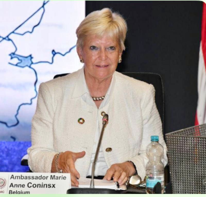 Eine Frau, die vor einem Mikrofon sitzt, unter ihr steht der Name Botschafterin Marie Anne Coninsx