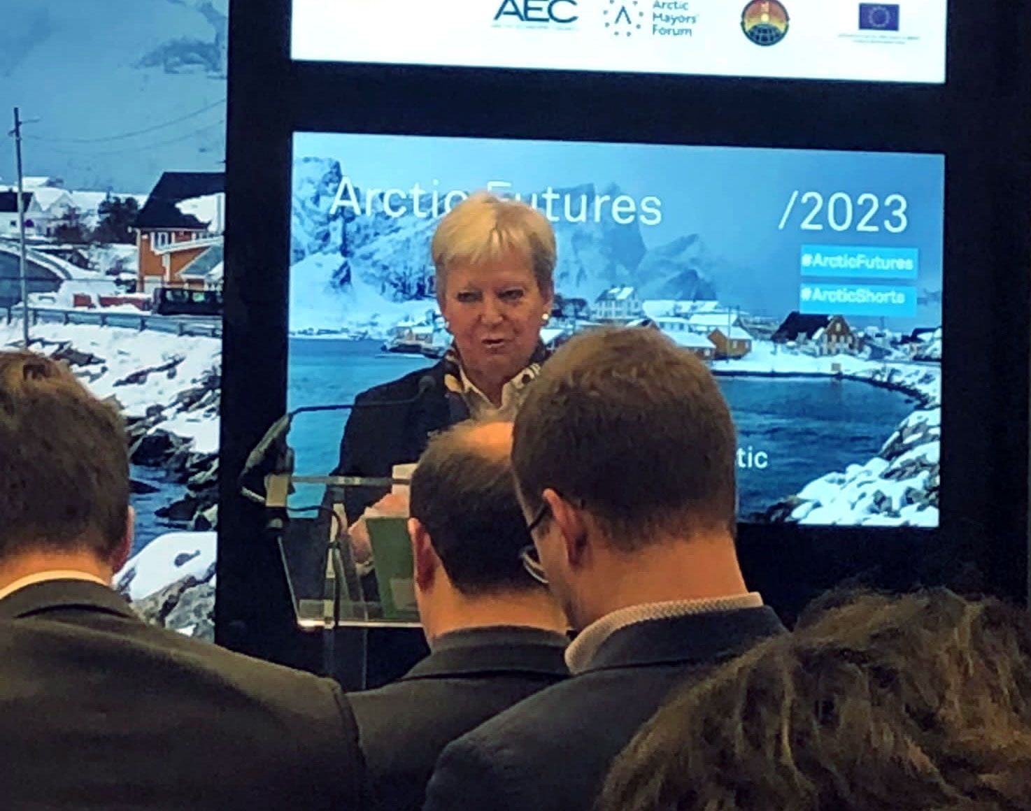 Eine Frau steht auf einem Podium vor einem Bildschirm mit der Aufschrift 2023