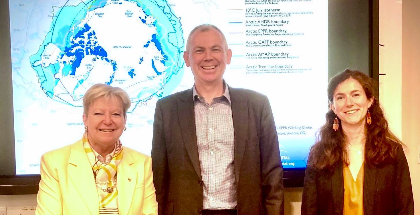 Ein Mann und zwei Frauen stehen nebeneinander vor einem großen Bildschirm.