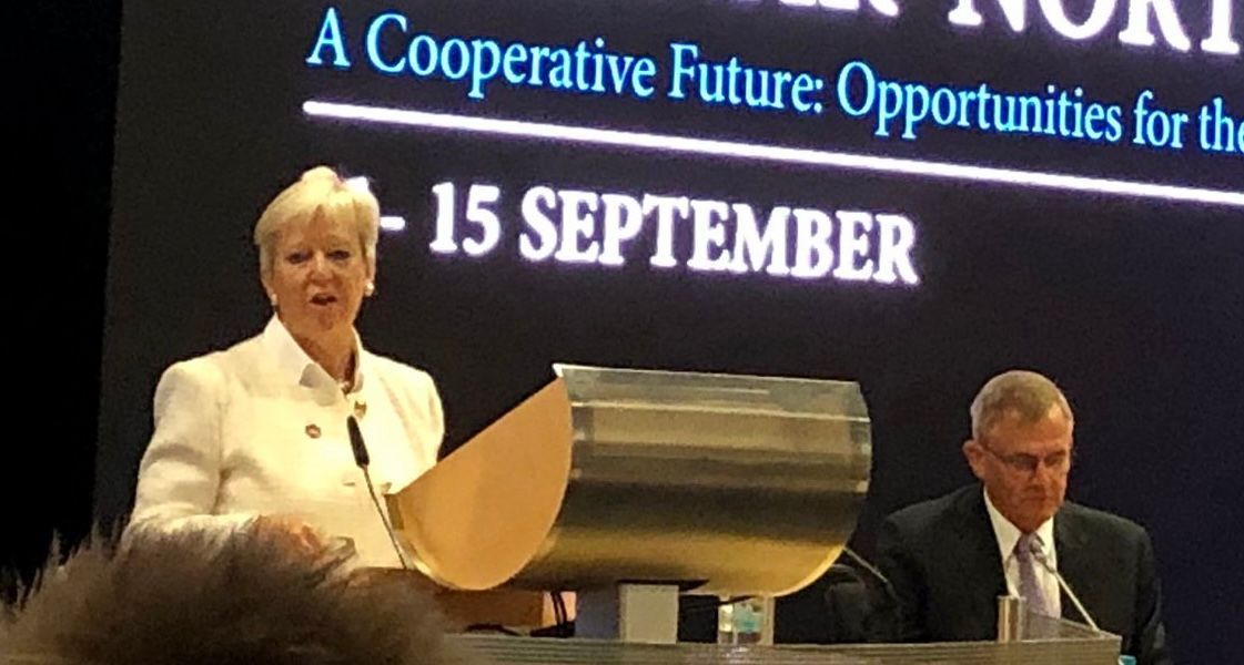 Eine Frau hält eine Rede vor einem Schild mit der Aufschrift „Kooperative Zukunftschancen für die Zukunft“