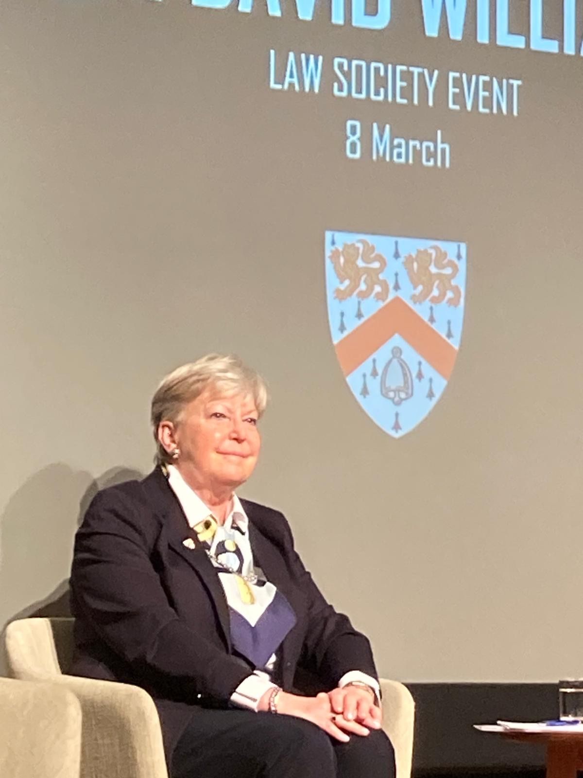Eine Frau sitzt vor einem Bildschirm, auf dem steht: Veranstaltung der Law Society am 8. März