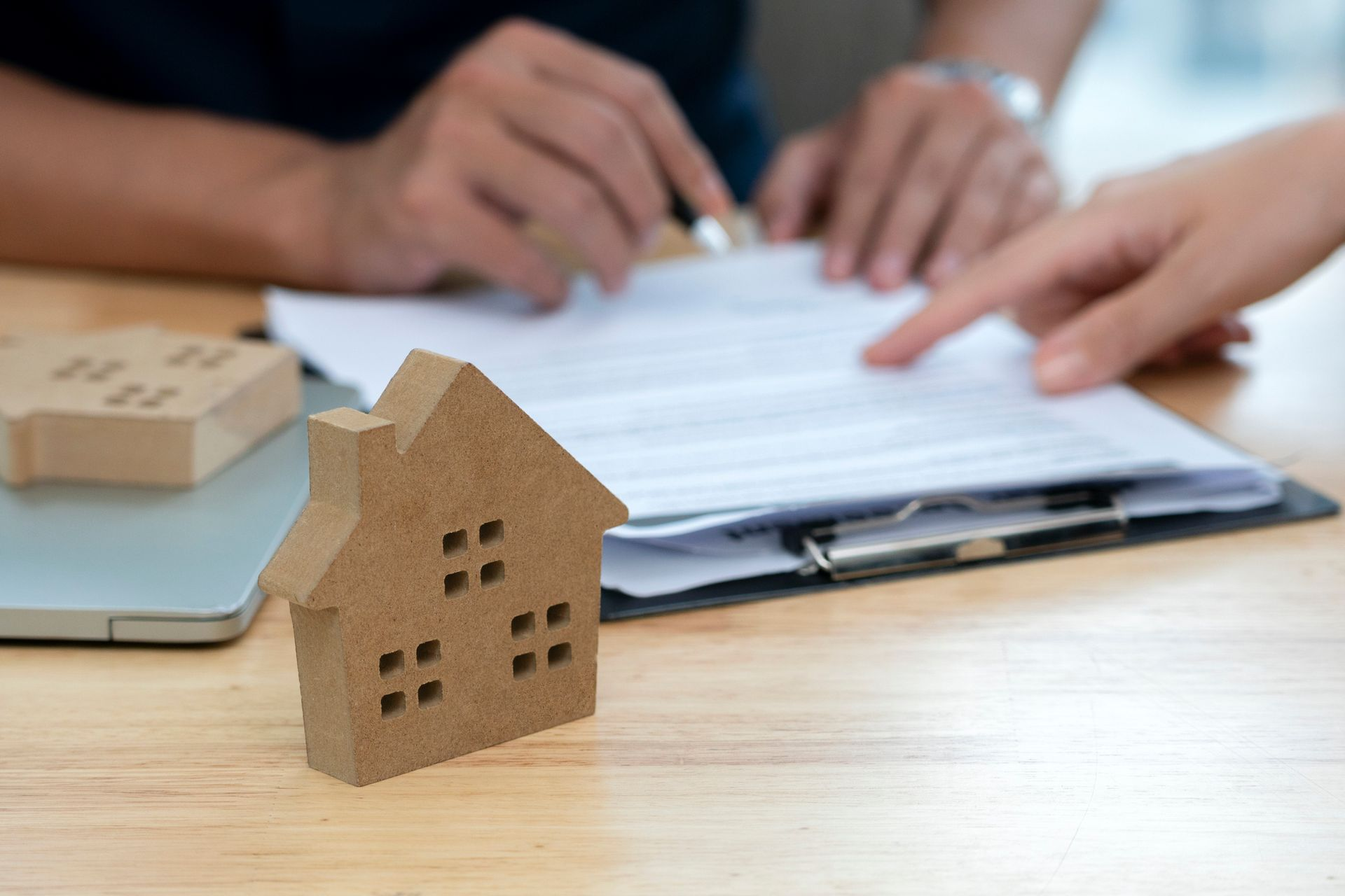 A wooden house is sitting on a wooden table next to a clipboard.