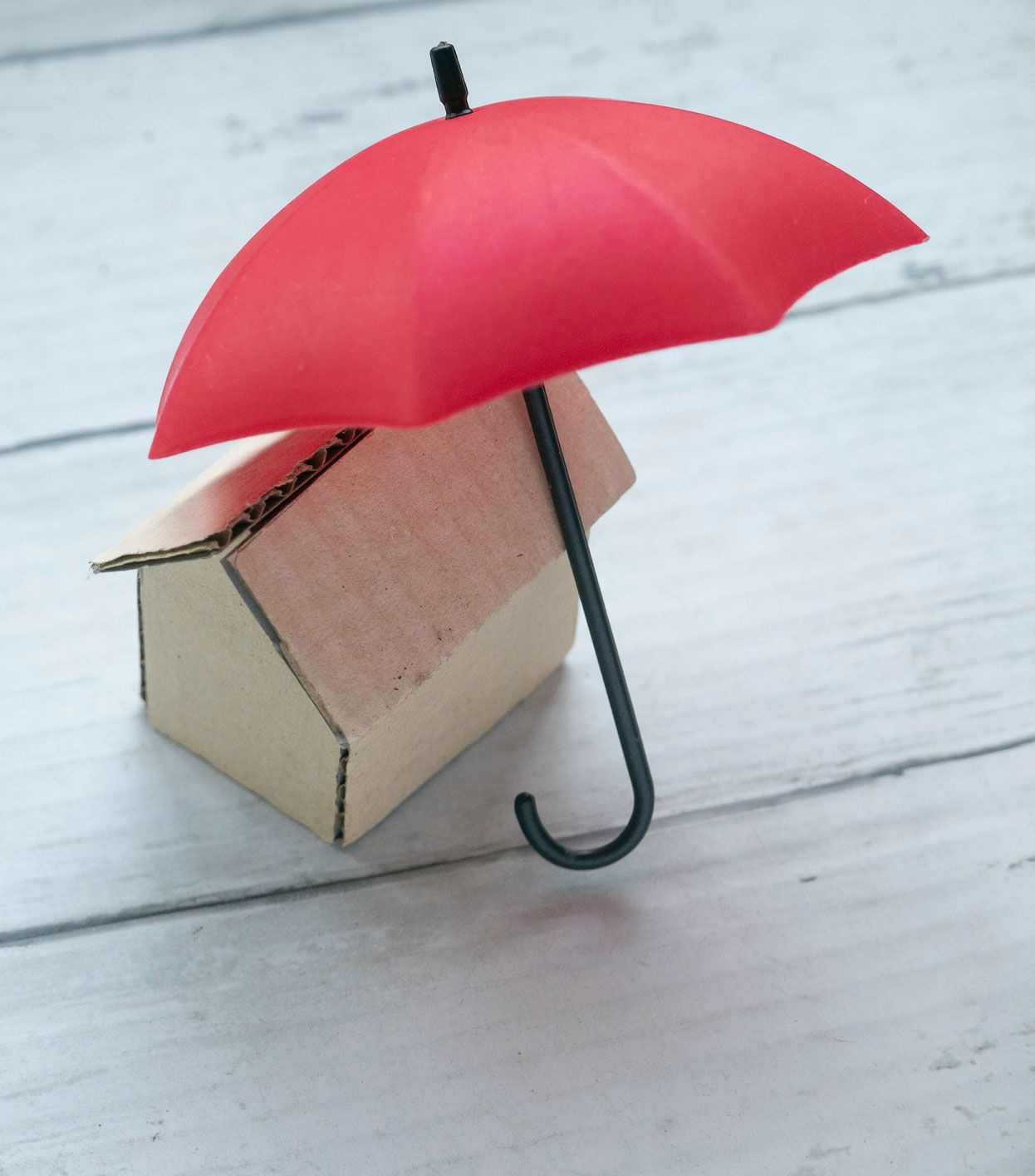 A small cardboard house with a red umbrella over it