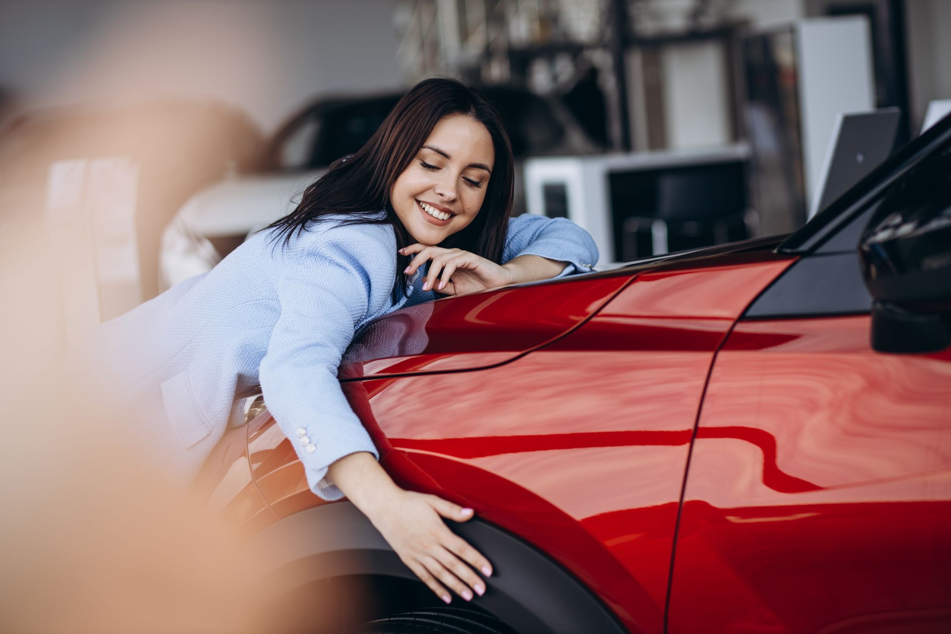 A woman is hugging a red car in a showroom.