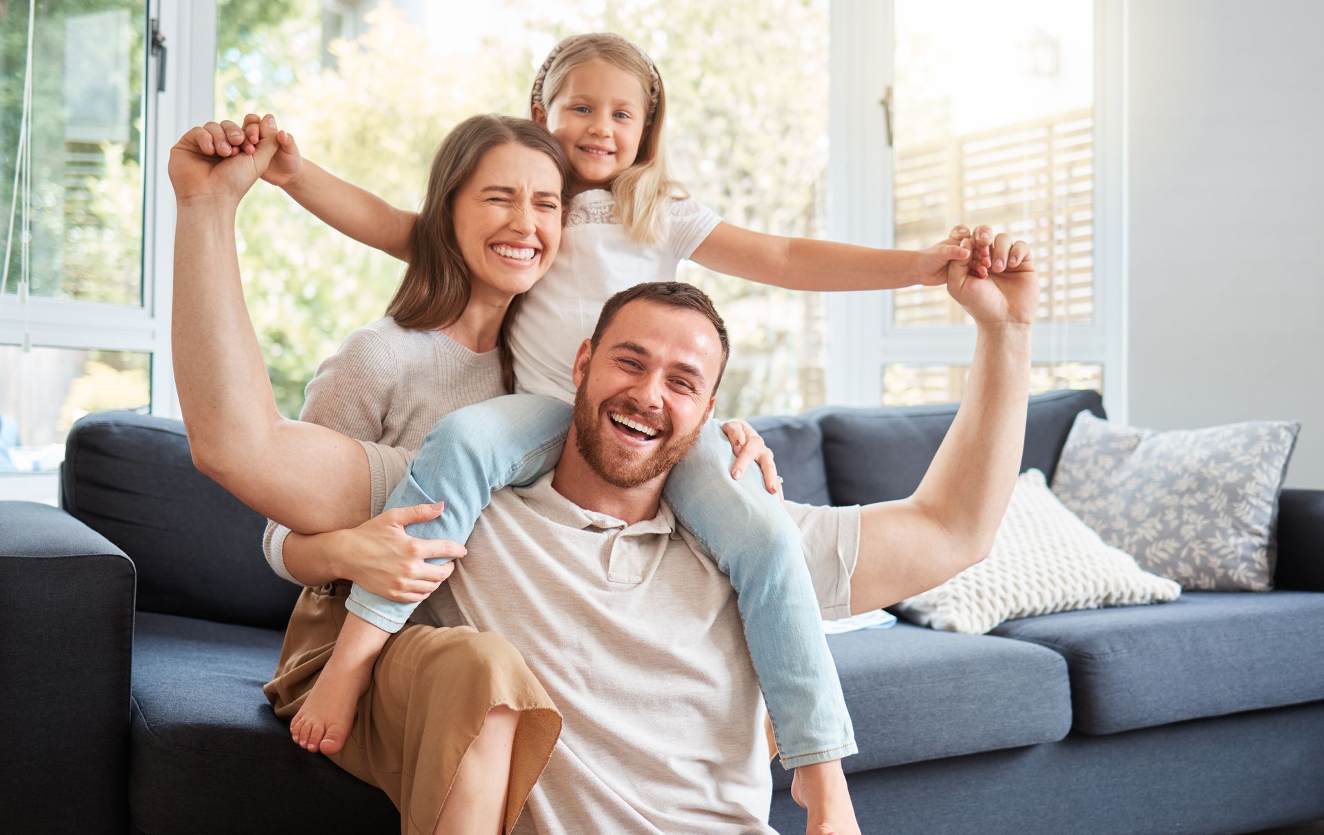 A man is sitting on a couch with his wife and daughter on his shoulders.