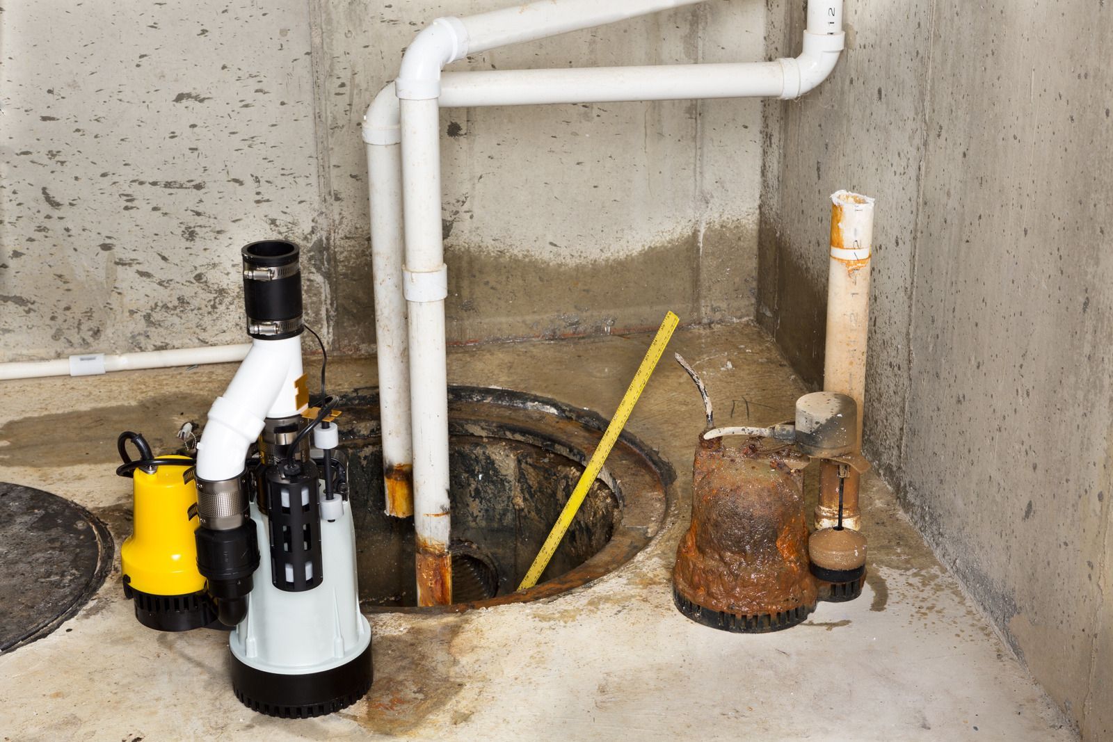 Sump pump system in a concrete basement. Includes pumps, pipes, and a pit, with some standing water.