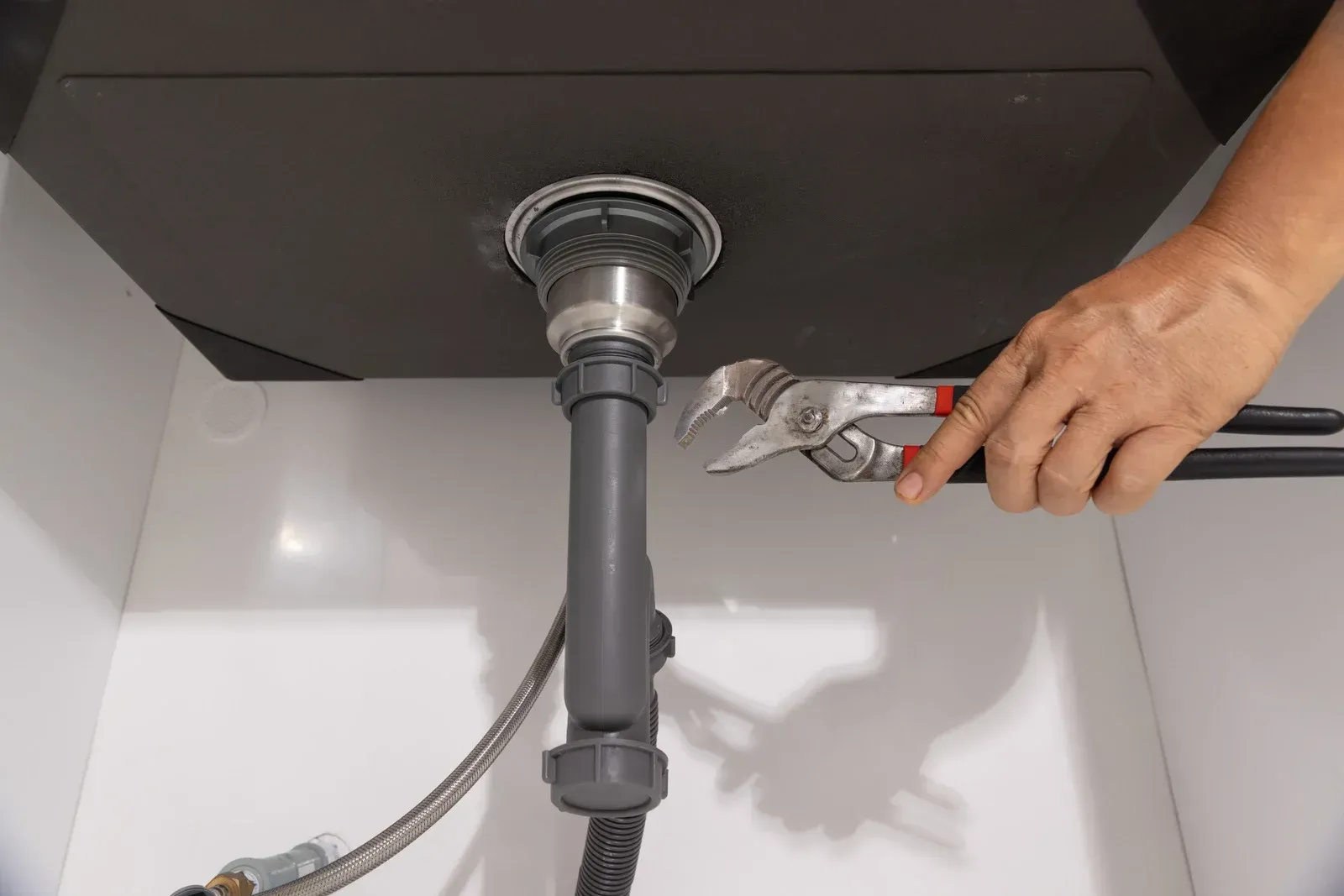 Person using a wrench to tighten a pipe under a kitchen sink.