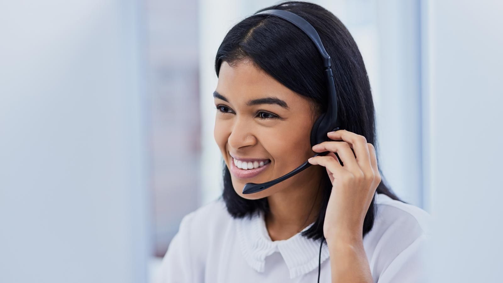 Woman wearing a headset, smiling, looking at a computer screen.