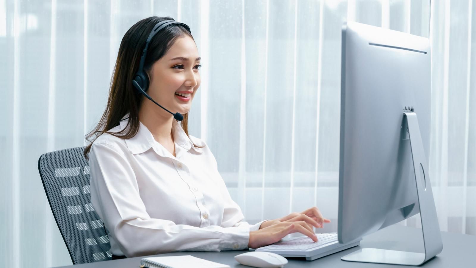 A receptionist wearing a headset is sitting in front of a computer.