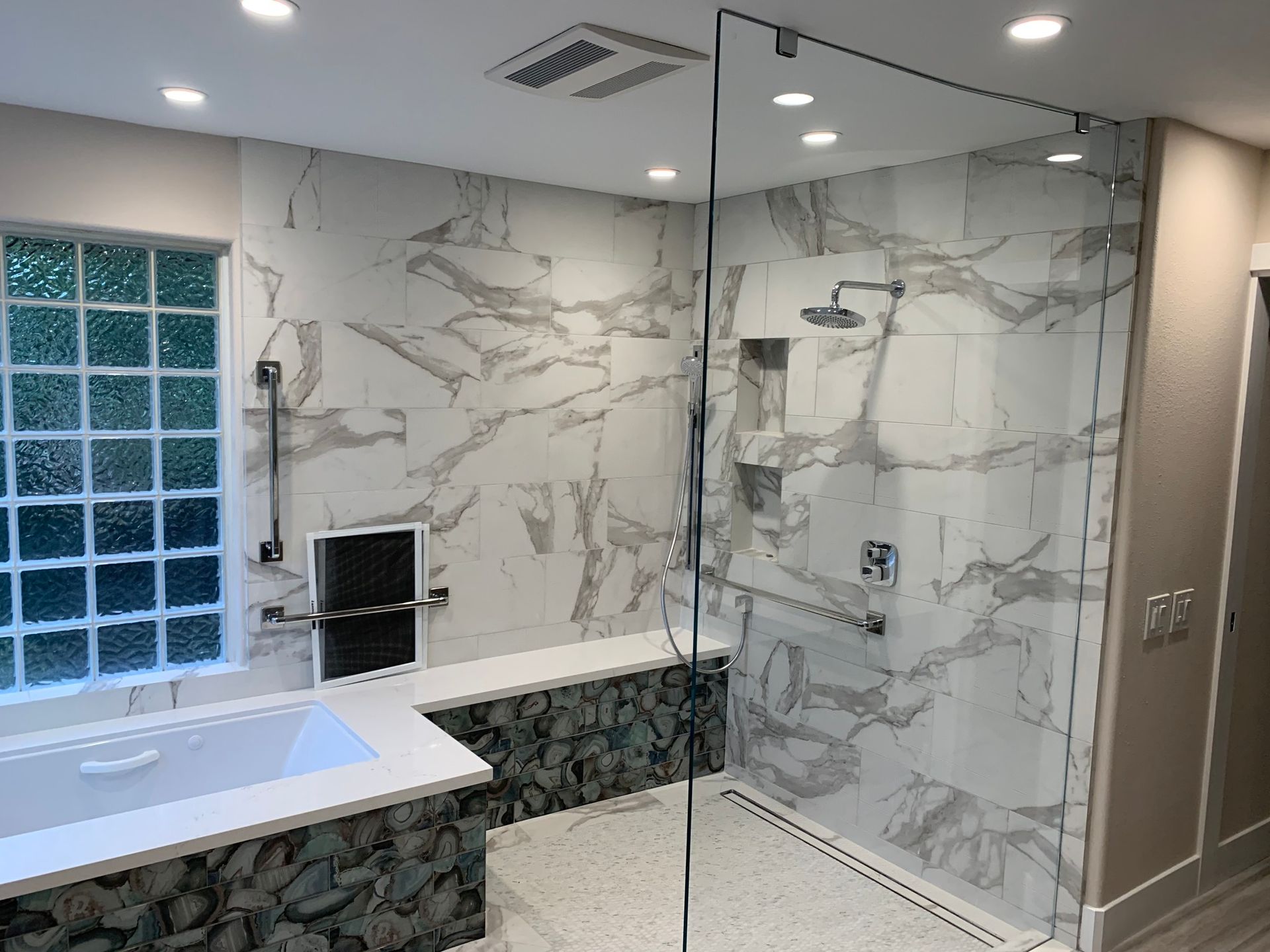 Modern bathroom with marble tile and glass shower enclosure.