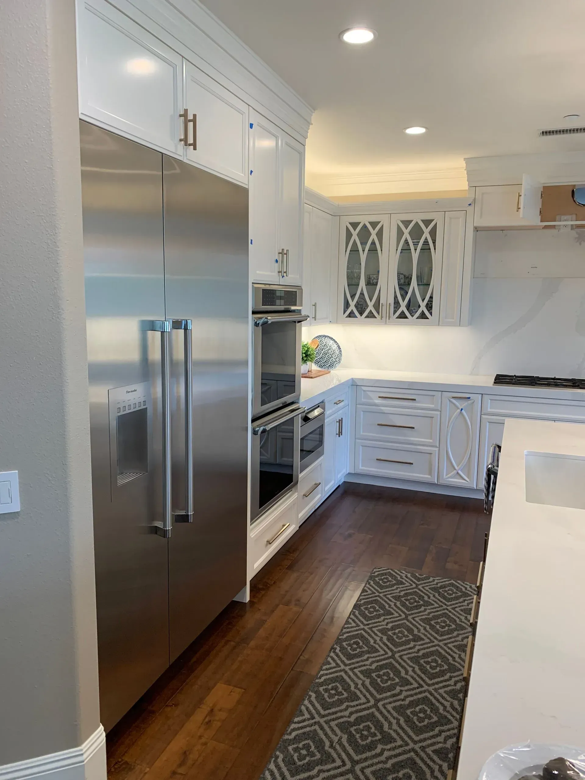 Kitchen with white cabinets, stainless steel refrigerator and oven, dark wood floor, and decorative rug.