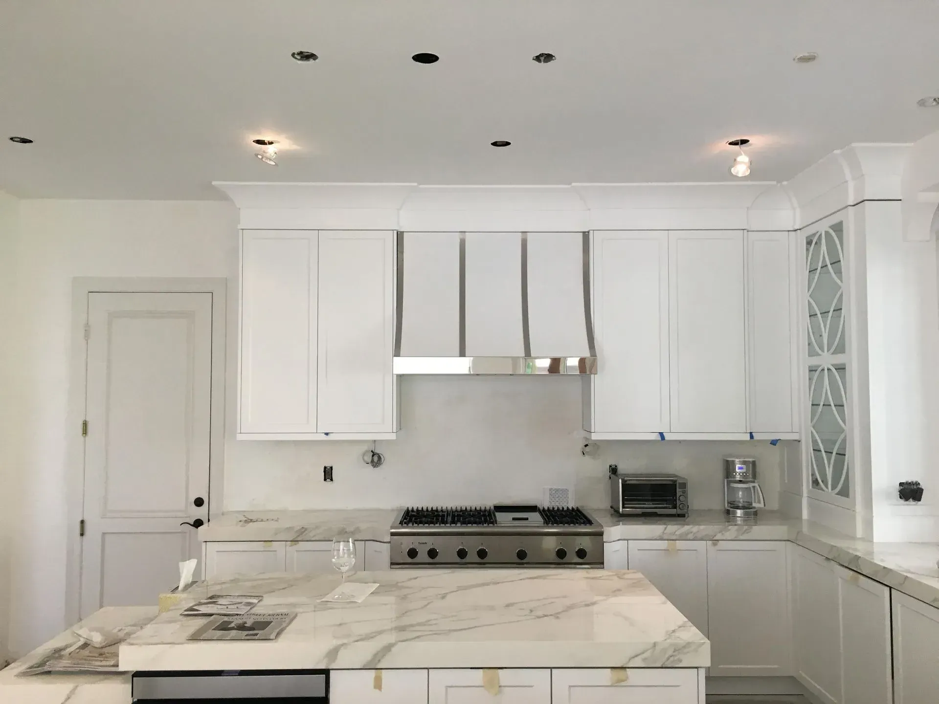 White kitchen with marble countertops, stainless steel appliances, and upper cabinets.