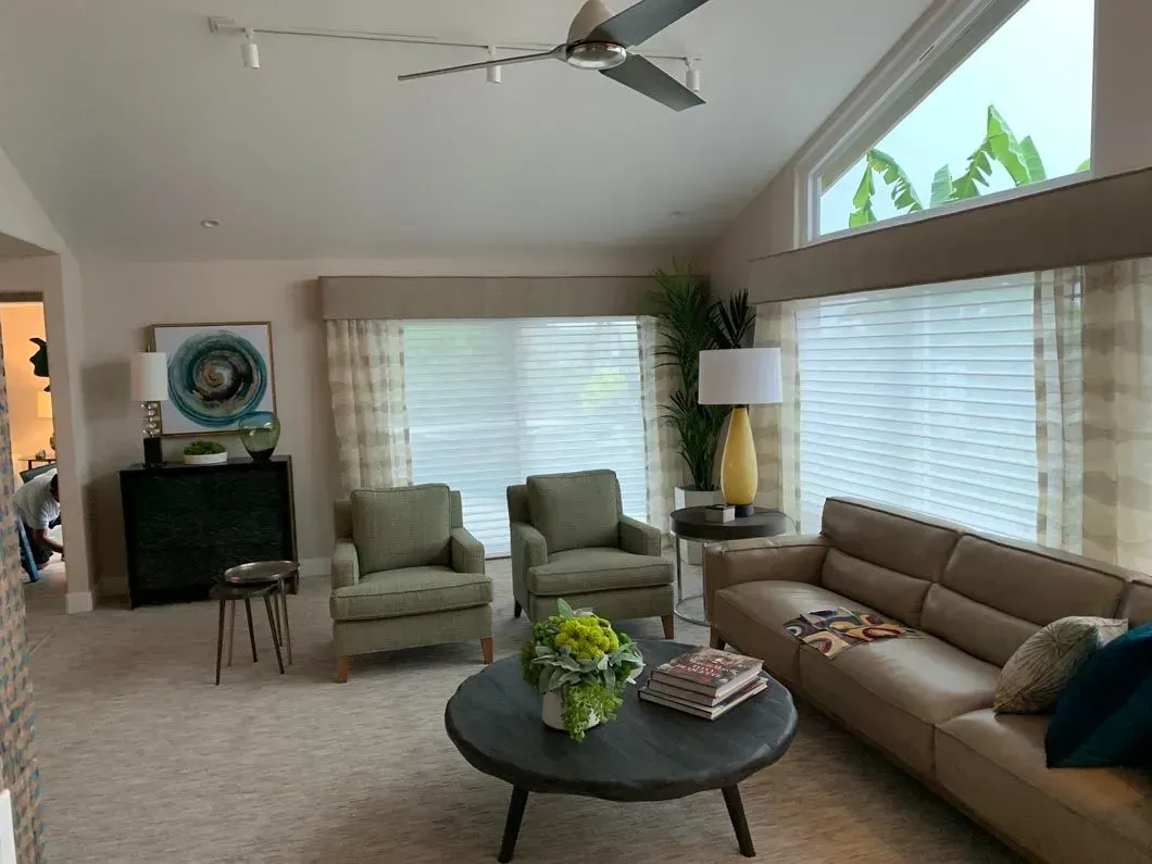 Living room with beige walls, a tan sofa, green armchairs, and a dark round coffee table.
