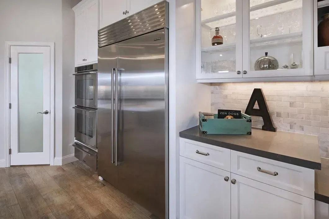 Modern kitchen with stainless steel refrigerator, white cabinets, and frosted glass door.