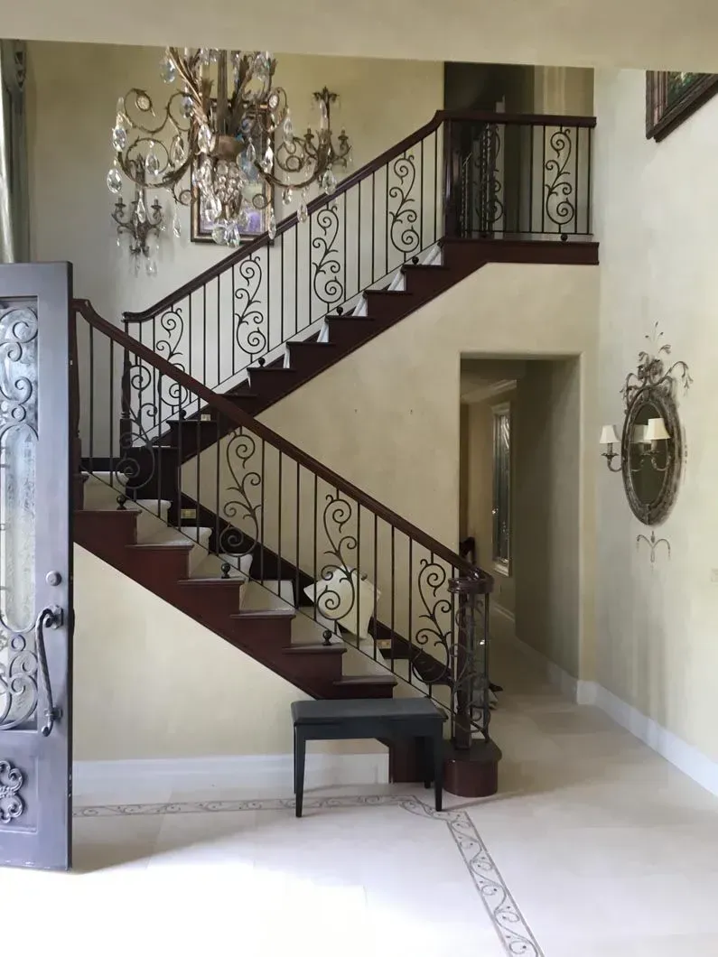 Ornate staircase with dark wood steps and railing, leading up to a second floor. A chandelier hangs above.