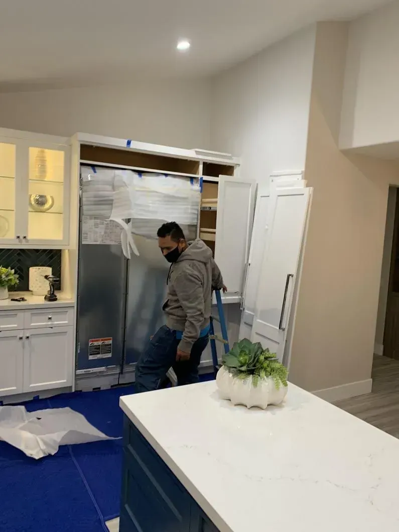 Man installing a refrigerator in a kitchen with white cabinets and an island.