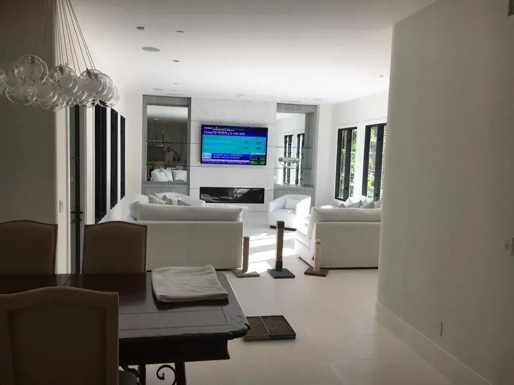 Living room with white walls, sofas, fireplace, and TV. Dining table in foreground.