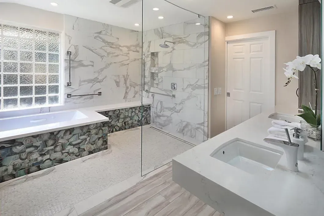 Modern bathroom with marble shower, white sink, and bathtub.