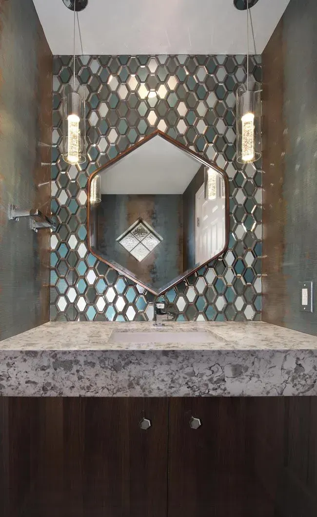 Bathroom with patterned tile backsplash, geometric mirror, pendant lights, and wooden cabinet.