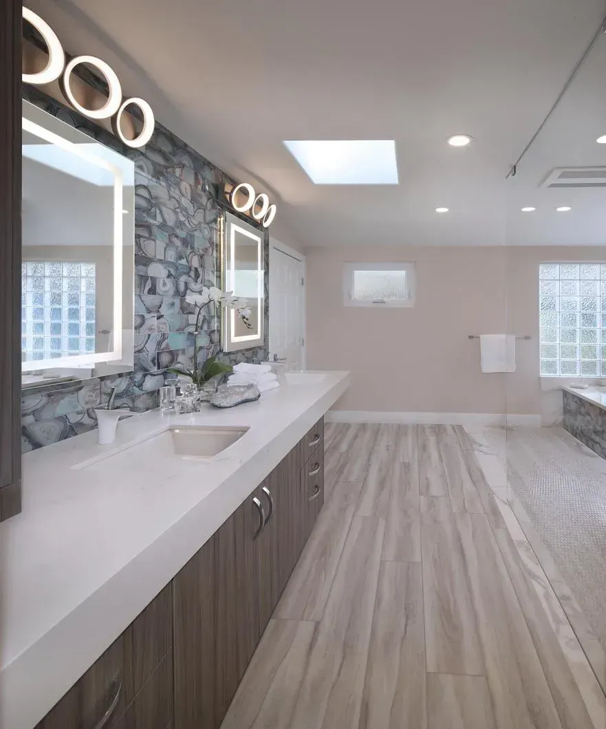 Spacious bathroom with long vanity, blue accent wall, and wood-look flooring. Natural light from a skylight.