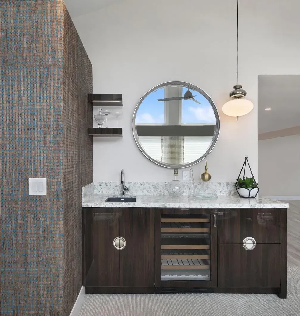 Dark wood bar with marble countertop, wine fridge, circular mirror, and textured accent wall.