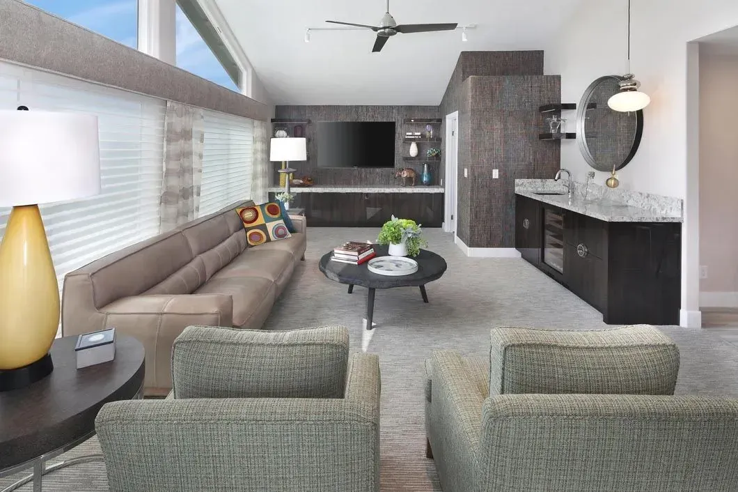 Modern living room with neutral colors, sofa, armchairs, bar, TV, and large windows.