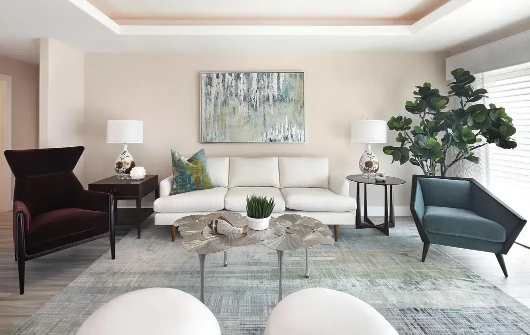 Living room with white sofa, accent chairs, blue-green rug, and artwork.