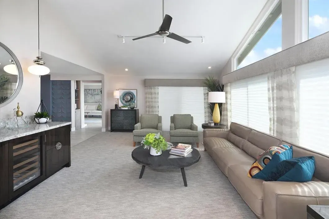 Spacious living room with tan sofa, green armchairs, dark bar, ceiling fan, and large windows.