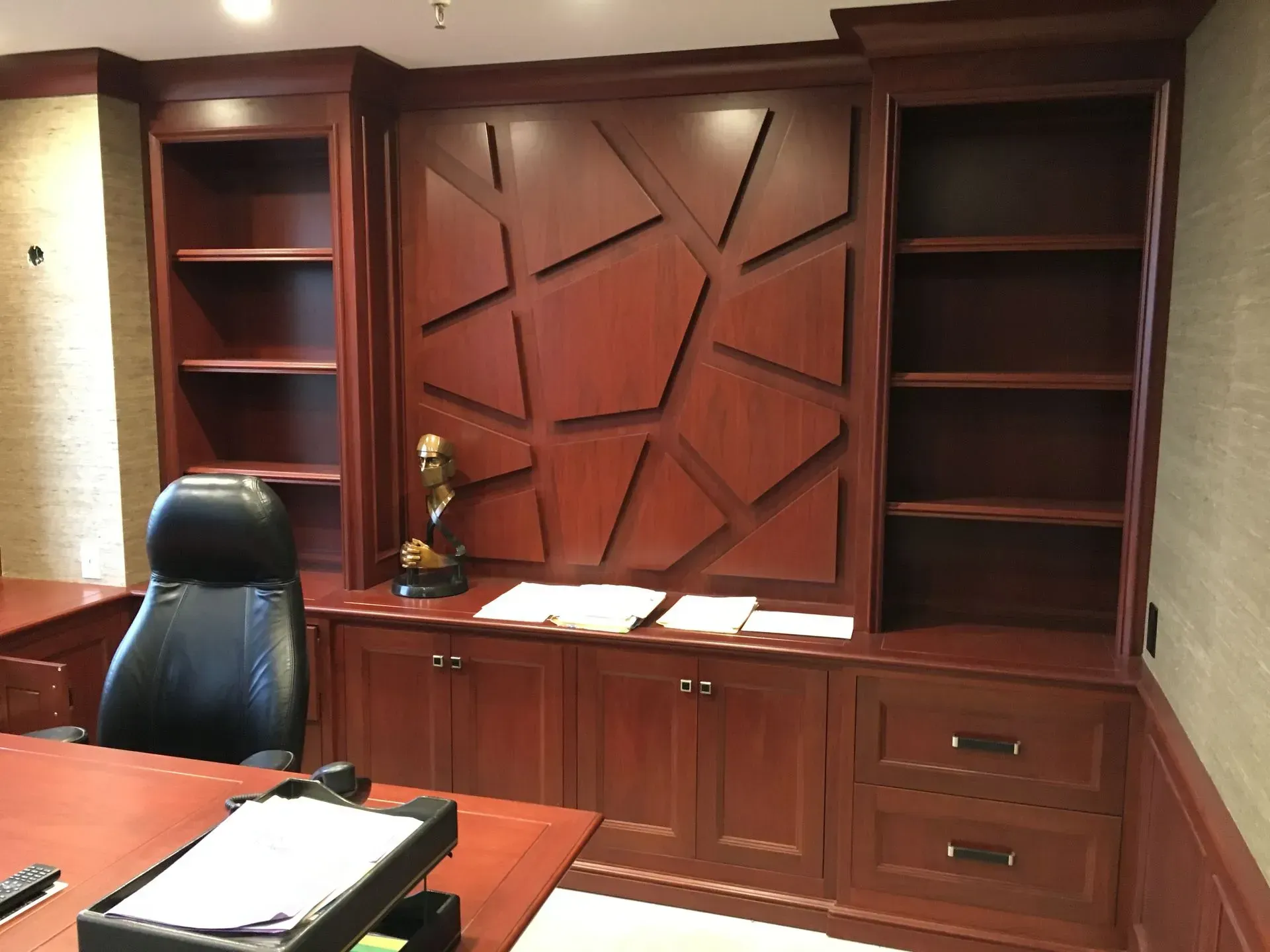 Dark wood office built-in with shelves, cabinets, desk, and a geometric pattern wall design.