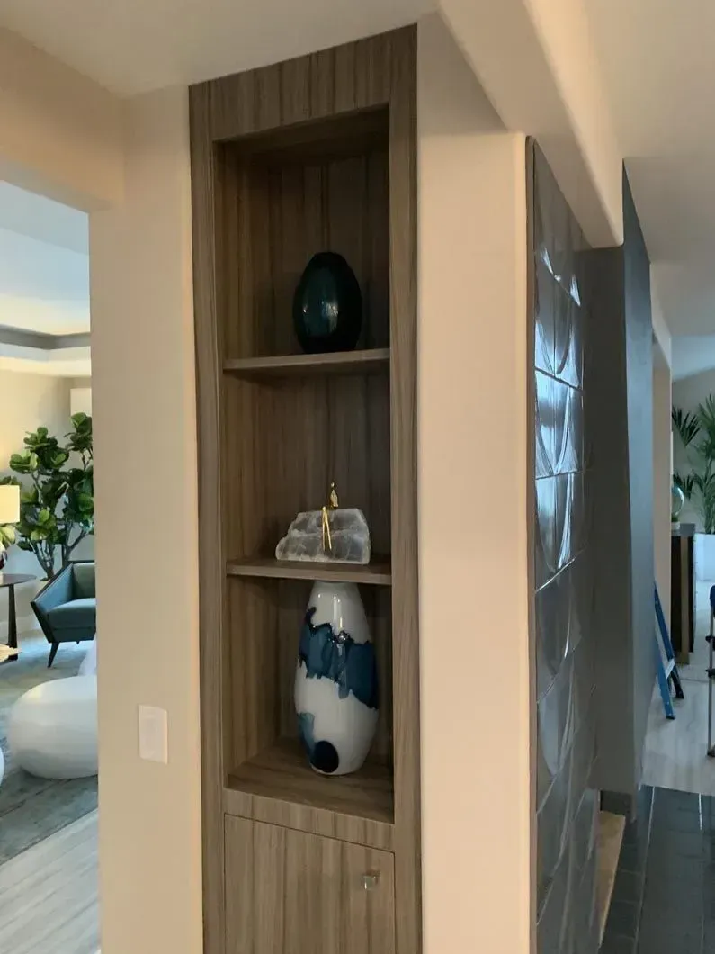 Built-in wooden shelves in a wall niche display decorative objects: a blue egg, stone sculpture, and vase.