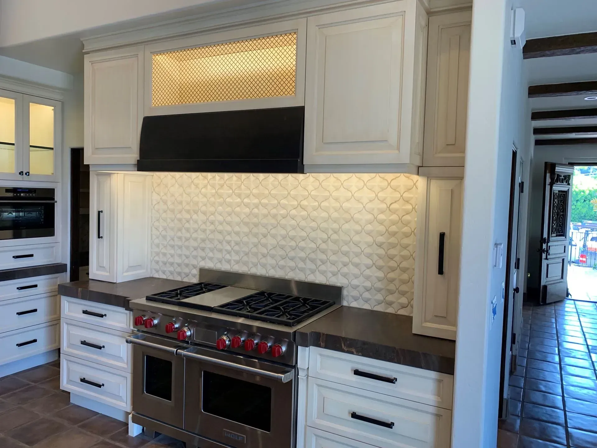 Kitchen with white cabinets, dark countertop, stove, and patterned backsplash.