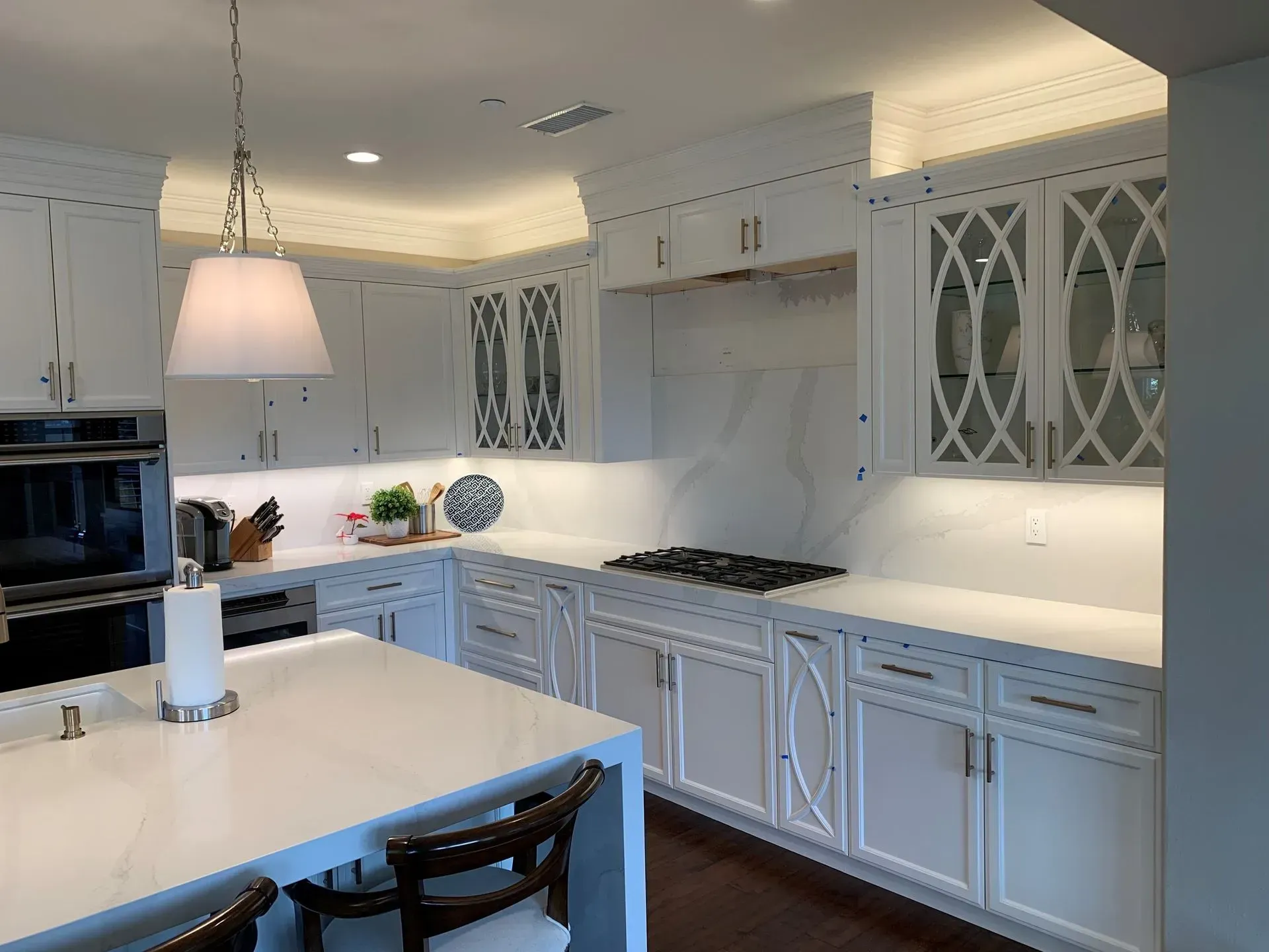 White kitchen with quartz countertops and cabinets, stainless steel appliances, and island with a pendant light.