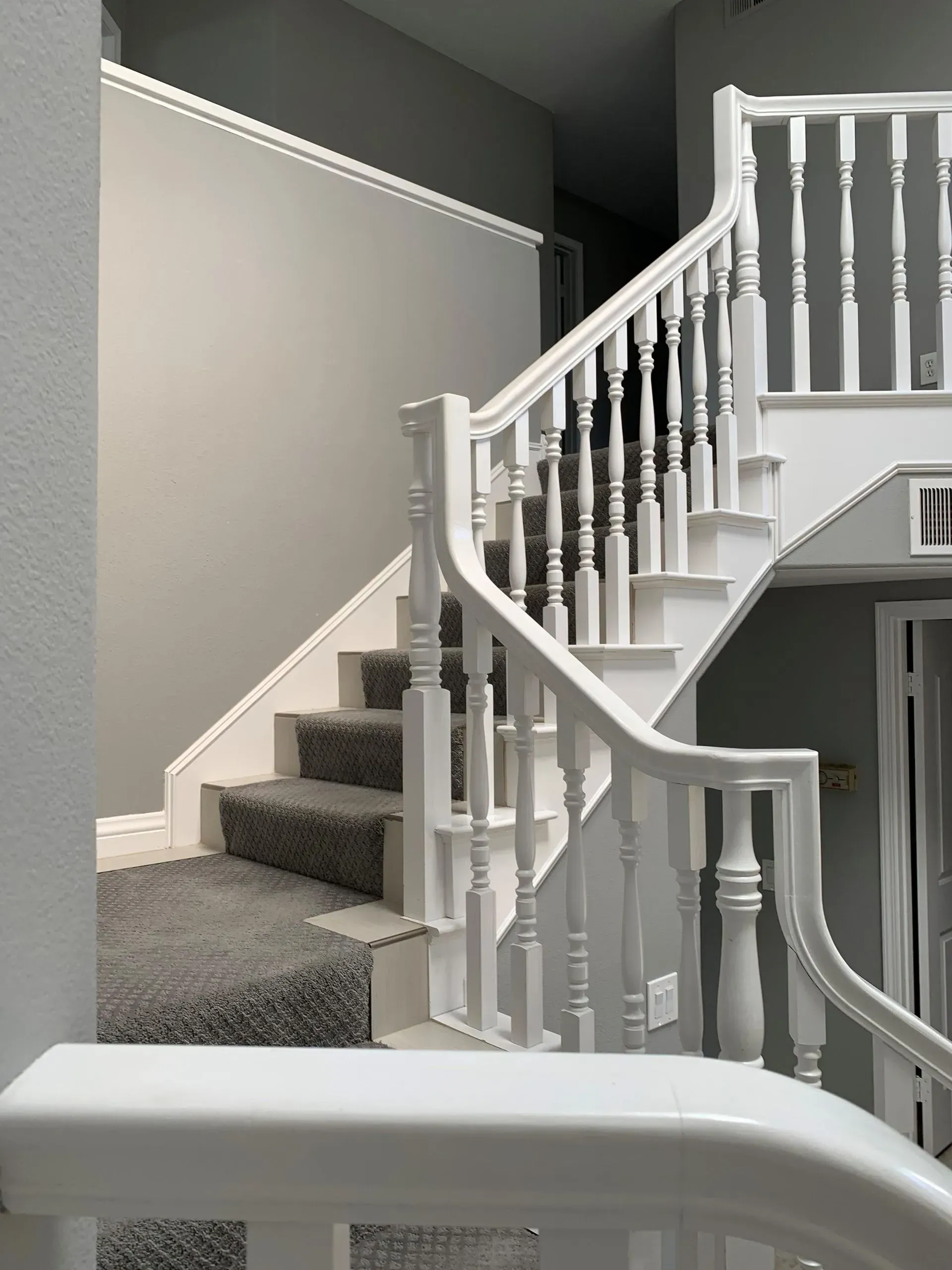 White staircase with carpeted steps, white balusters, and gray walls.