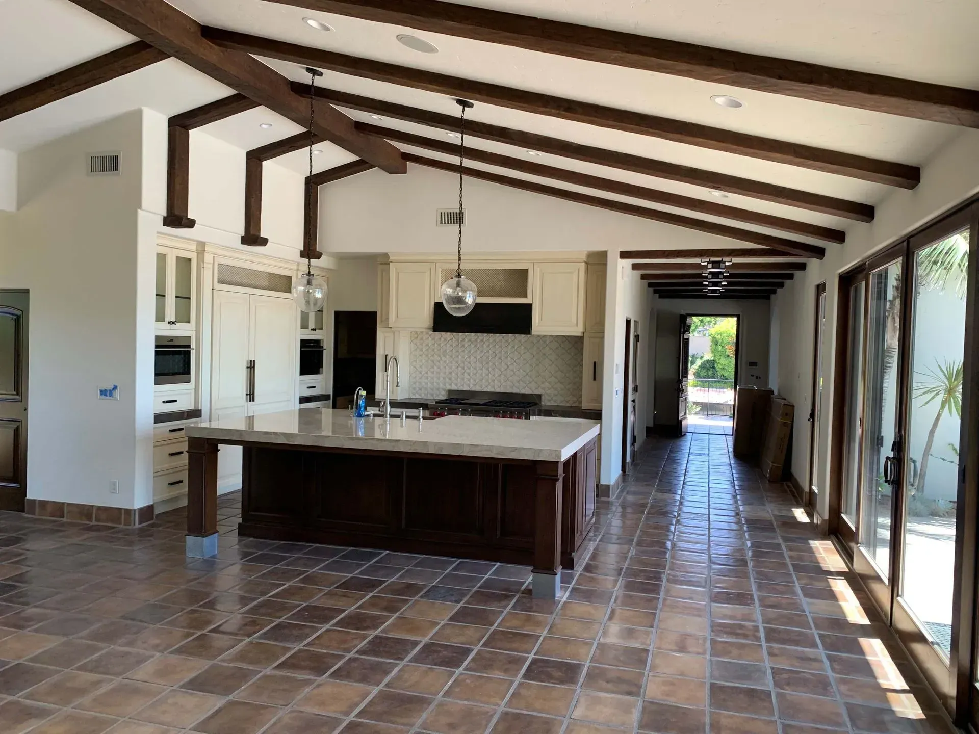 Spacious kitchen with dark wood beams, beige cabinets, large island, and terracotta tile floor.