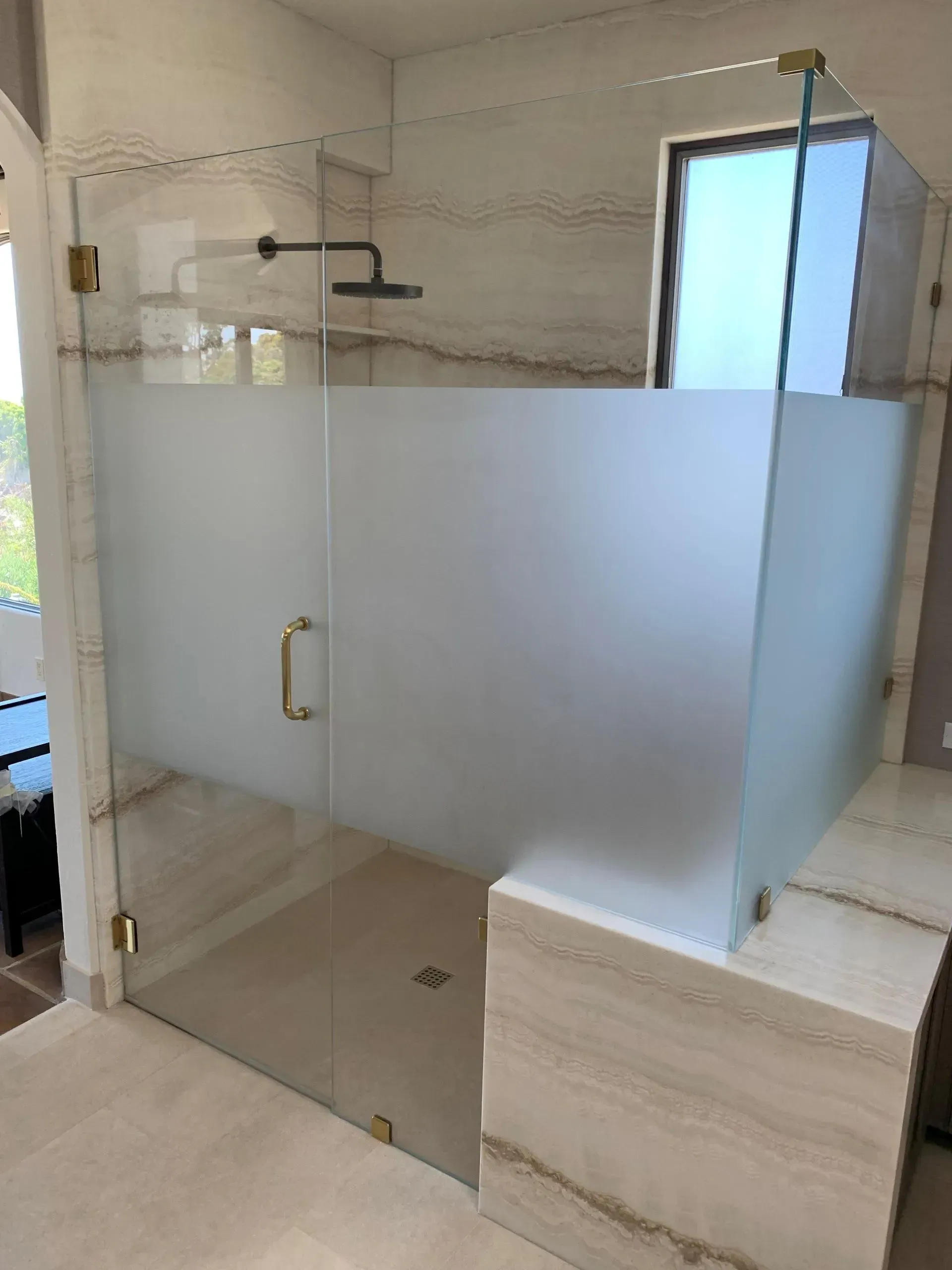 Glass shower with frosted privacy panel, gold hardware, and beige tile.