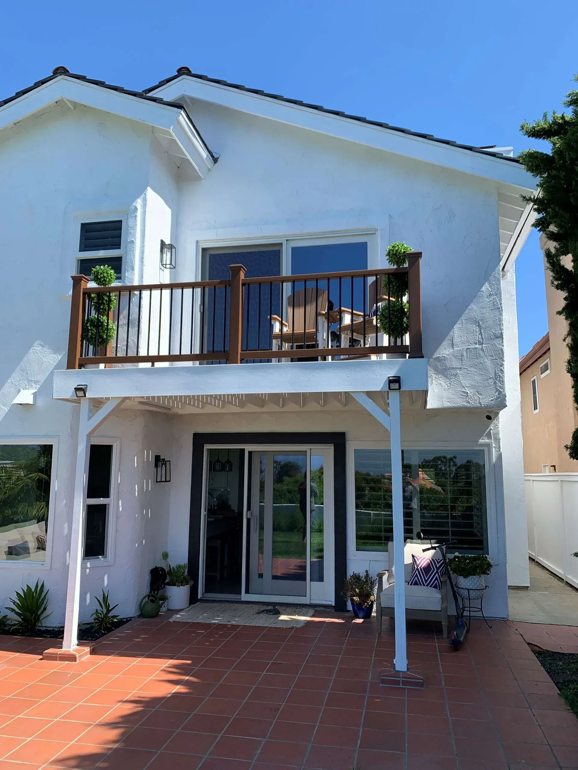 Two-story white house with a brown tile patio and a balcony overlooking the backyard.
