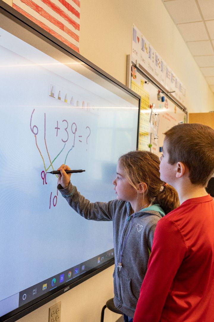 A boy and a girl are working on a math problem on a whiteboard