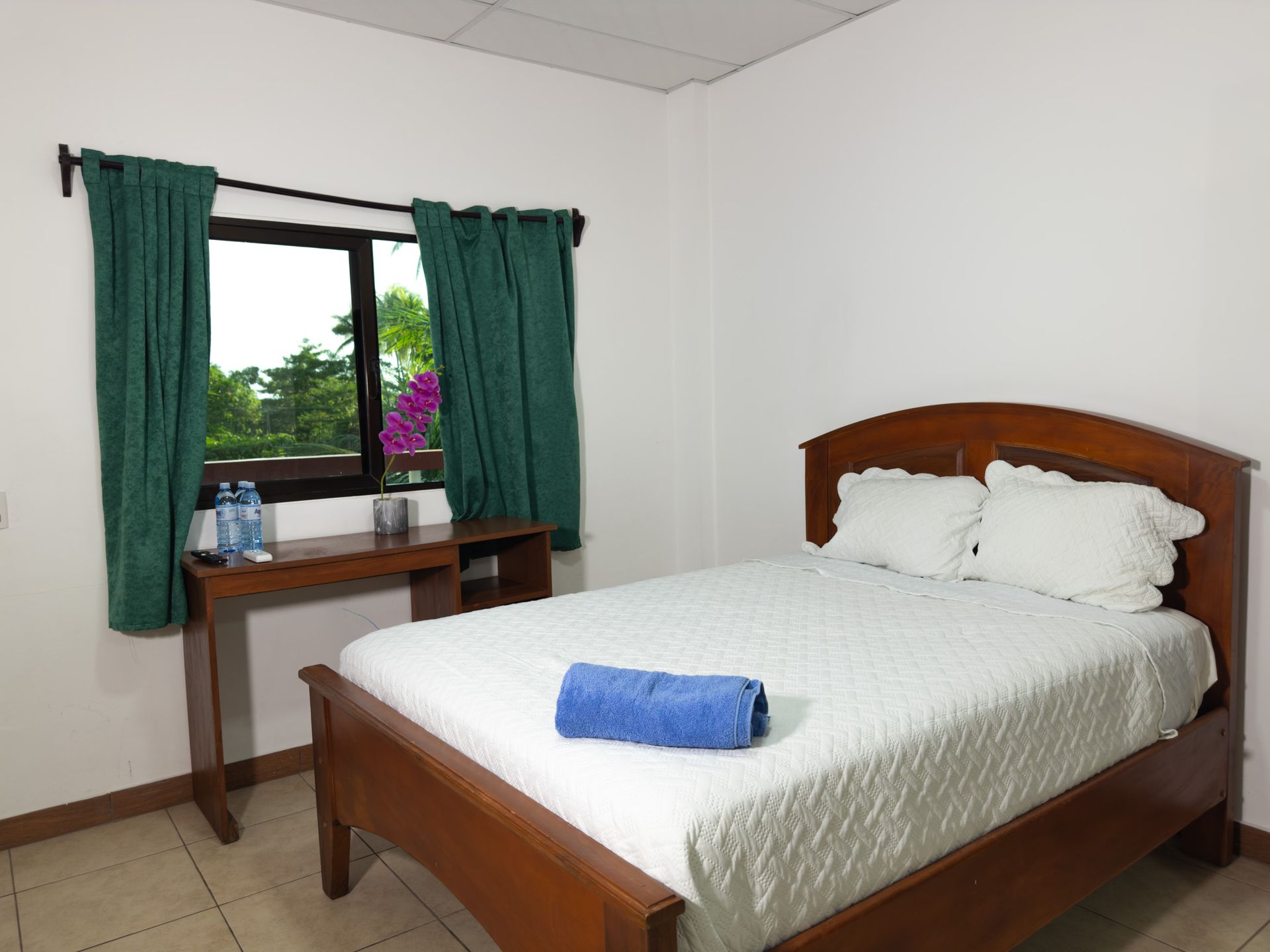 Bedroom with wooden bed, desk, and window with green curtains.